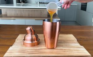 Scoop of passionfruit fruit mix being poured into a rose gold cocktail shaker