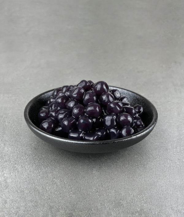 Cooked, dark purple Blueberry tapioca fruit pearls in a small black ceramic dish