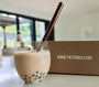 Cold Pearl Milk Bubble Tea with brown pearls, rose gold stainless steel straw. In front of a The Tea Box branded box