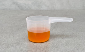 A plastic scoop filled to the third line from the bottom with passionfruit fruit mix