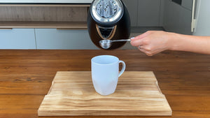 Adding 2 tablespoons of hot water from a kettle into a white mug holding taro powder