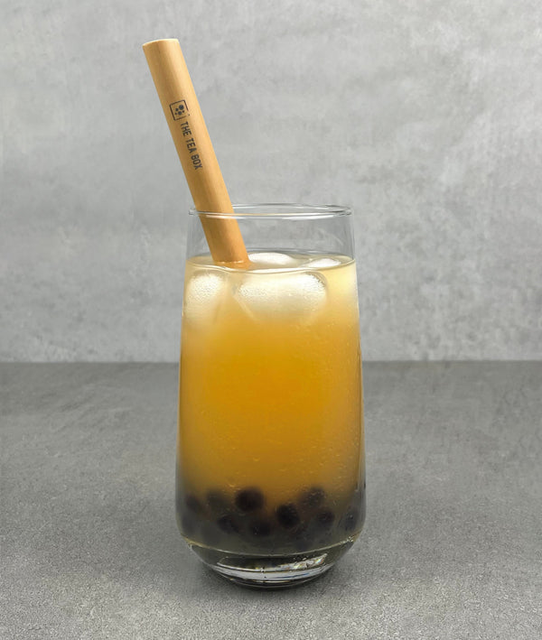 A glass of Lychee Bubble Tea with Blueberry pearls, ice and a reusable bamboo bubble tea straw