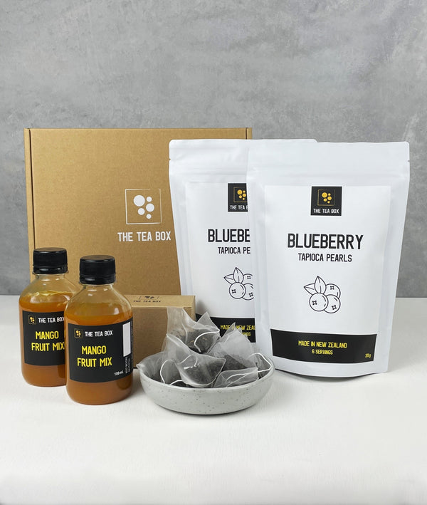 Contents of 12 pack Mango Bubble Tea Kit. Blueberry pearls in pouches, bottles of fruit mix, tea bags, scoop and cardboard gift box