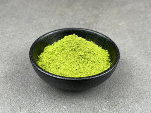 Vibrant green matcha powder in a round black ceramic dish