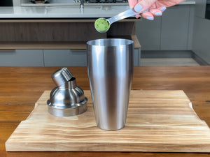 One teaspoon of bright green matcha powder about to be added to a stainless steel shaker