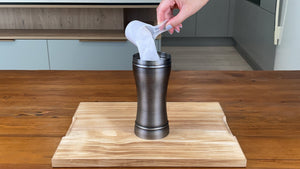 Milk tea powder in a plastic scoop being added to an antique grey stainless steel cocktail shaker