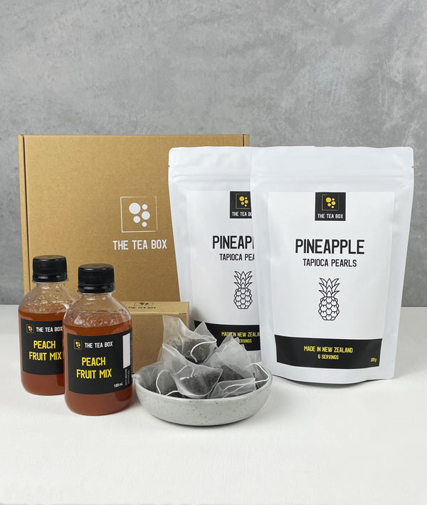 Contents of 12 pack Peach Bubble Tea Kit. Pineapple pearls in pouches, bottles of fruit mix, tea bags, scoop and cardboard gift box