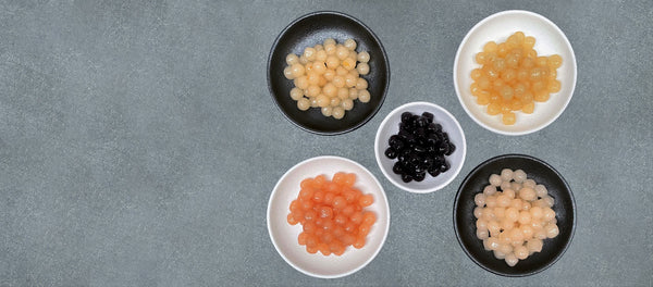 5 small black and white ceramic dishes containing brightly coloured cooked fruit pearls. Yuzu, Pineapple, Lychee, Blueberry and Red Grapefruit