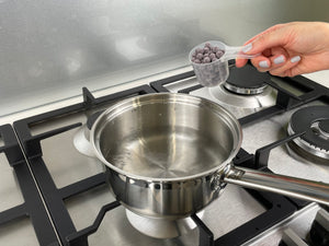 Uncooked, dark purple Blueberry tapioca fruit pearls in a plastic scoop about to be added to a small pot of boiling water