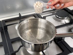 Uncooked, pink-coloured Red Grapefruit tapioca fruit pearls in a plastic scoop about to be added to a small pot of boiling water
