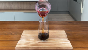 Freshly brewed black tea being poured into serving glass holding brown tapioca pearls