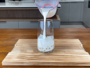 Half a glass of cold milk being poured over the ice cubes and cooked pearls