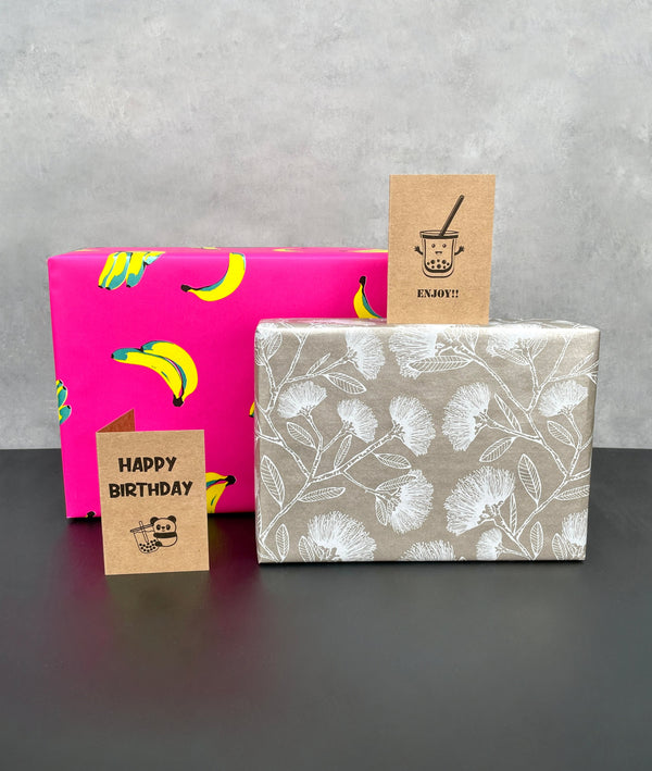 2 gift wrapped boxes. Bananas with green metallic shadows on bright pink background, white Pohutukawa on silver background and 2 brown kraft cards