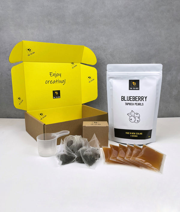 Contents of a 6 pack Lychee Bubble Tea Kit. Blueberry pearls in a pouch, sachets of Lychee fruit mix, tea bags, scoop and cardboard gift box