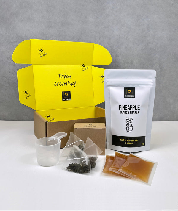 Contents of a 3 pack Lychee Bubble Tea Kit. Pineapple pearls in a pouch, sachets of Lychee fruit mix, tea bags, scoop and cardboard gift box