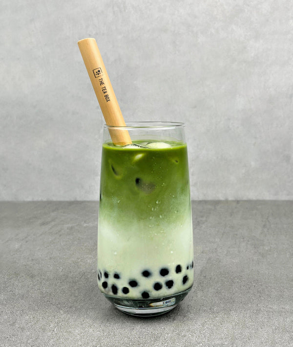 A glass of cold Matcha Latte Bubble tea with Blueberry pearls, ice and a reusable bamboo bubble tea straw