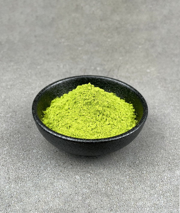 Small black ceramic dish filled with vibrant green 100% pure organic Matcha powder