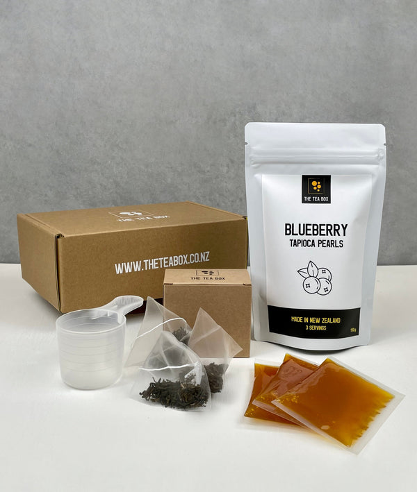 Contents of a 3 pack Passionfruit Bubble Tea Kit. Blueberry pearls in a pouch, sachets of Passionfruit fruit mix, tea bags, scoop and cardboard gift box