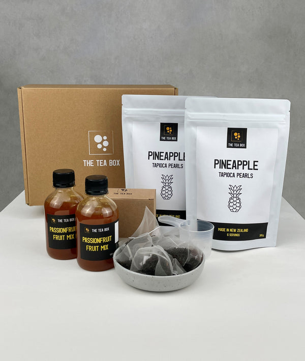 Contents of a 12 pack Passionfruit Bubble Tea Kit. Pineapple fruit pearls in pouches, bottles of Passionfruit fruit mix, tea bags, scoop and cardboard gift box