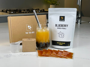 Glass of Passionfruit Bubble Tea with Blueberry pearls, silver straw. Displayed with contents of a Fruit Bubble Tea Kit
