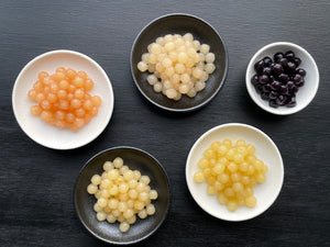 Ceramic dishes containing brightly coloured cooked fruit pearls. Yuzu, Pineapple, Lychee, Blueberry and Red Grapefruit