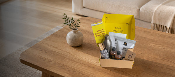 A fruit bubble tea kit on a wooden coffee table in a modern living room. The kit is open, showing the bright yellow inside of the box. Inside the kit is fruit mix, yuzu fruit pearls, bamboo straws, tea bags, cooking instructions and a cocktail shaker
