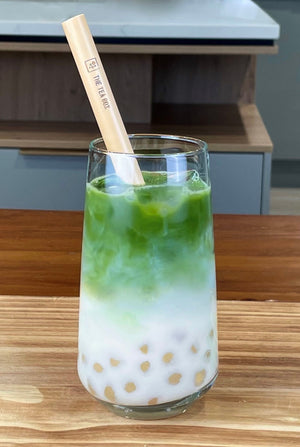 A glass of cold Matcha Latte Bubble Tea with pink-coloured, Red Grapefruit tapioca fruit pearls, ice and a reusable bamboo bubble tea straw