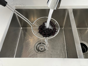 Cooked, dark purple Blueberry tapioca fruit pearls in a metal sieve being rinsed under cold running water