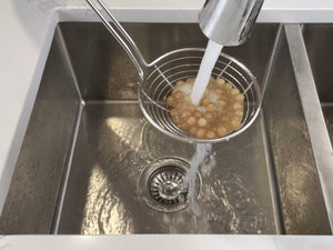 Cooked light pink tapioca fruit pearls in a strainer being rinsed under cold running water