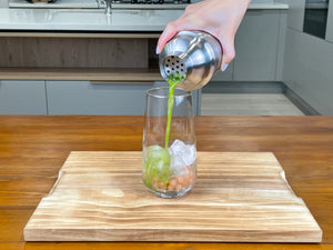Vibrant green Matcha Yuzu tea being poured from a stainless steel shaker into a glass holding cooked, pink-coloured Red Grapefruit tapioca fruit pearls and ice