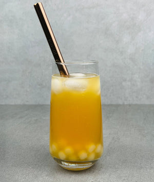 A glass of Mango Bubble Tea with Pineapple pearls, ice and a rose gold stainless steel straw