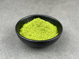 Vibrant green matcha powder in a round black ceramic dish