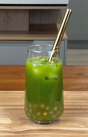 A glass of vibrant green Matcha Yuzu Bubble Tea with Red Grapefruit tapioca fruit pearls, ice and a gold stainless steel bubble tea straw