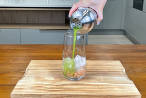 Bright green matcha tea being poured from stainless steel shaker into a glass containing Red Grapefruit tapioca pearls and ice