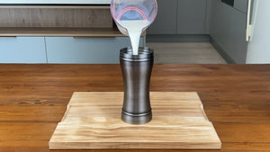 Three quarters of a cup of milk being poured into an antique grey stainless steel cocktail shaker