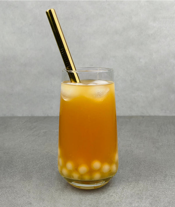 A glass of Peach Bubble Tea with Lychee pearls, ice and a gold stainless steel straw