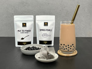 Pearl Milk Bubble Tea with Brown Tapioca Pearls and gold stainless steel straw. Displayed with pouches of milk tea powder and brown tapioca pearls. Round ceramic dishes holding cooked brown pearls and tea bags