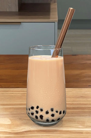 A glass of chilled Pearl Milk Bubble Tea with brown tapioca pearls and a rose gold stainless steel bubble tea straw