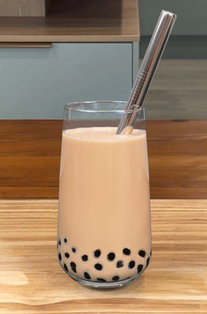 A glass of warm Pearl Milk Bubble Tea with brown tapioca pearls and a silver stainless steel bubble tea straw