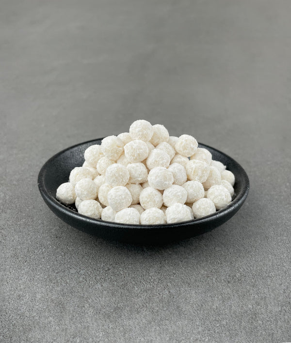 Uncooked Pineapple tapioca fruit pearls in a small black ceramic dish