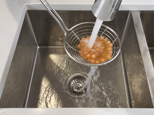 Cooked pink-coloured Red Grapefruit tapioca fruit pearls in a metal strainer being rinsed under cold running water