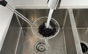 Cooked dark purple Blueberry tapioca fruit pearls in a metal strainer being rinsed under cold running water