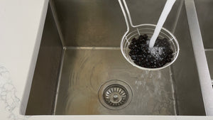 Cooked tapioca pearls in a metal strainer being rinsed under cold running water