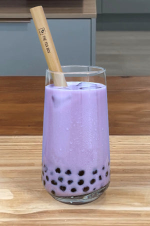 A glass of vibrant purple Taro Bubble Tea with brown tapioca pearls, ice cubes and a reusable bamboo bubble tea straw