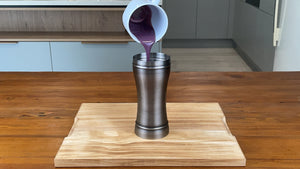 Vibrant purple taro mixture being poured into an antique grey stainless steel cocktail shaker