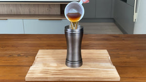 Freshly brewed black tea being poured from a white cup into an antique grey stainless steel cocktail shaker