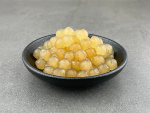 Cooked yellow Yuzu tapioca fruit pearls in a round black ceramic dish
