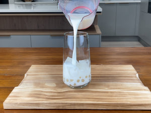 Half a glass of cold milk being poured over the ice cubes and cooked pearls 