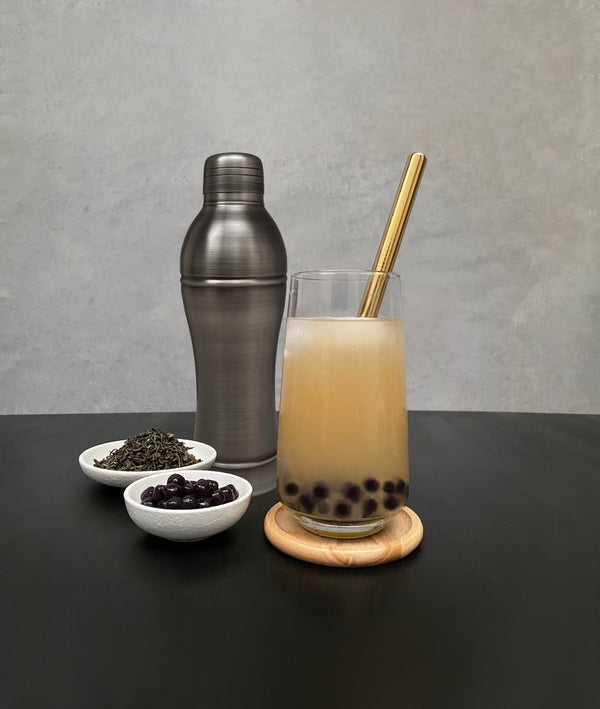 Dark antique grey shaker displayed with Lychee Bubble tea with Blueberry pearls, gold stainless steel straw, tea leaves, cooked Blueberry pearls