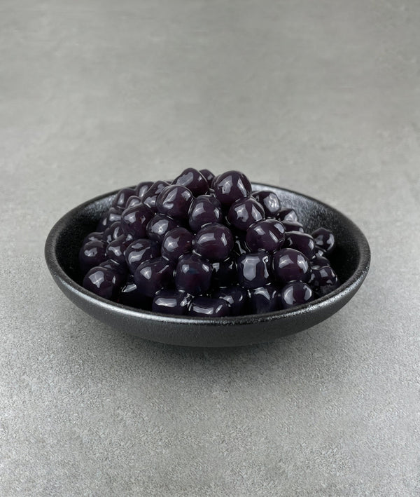 Cooked, dark purple Blueberry tapioca fruit pearls in a small black ceramic dish